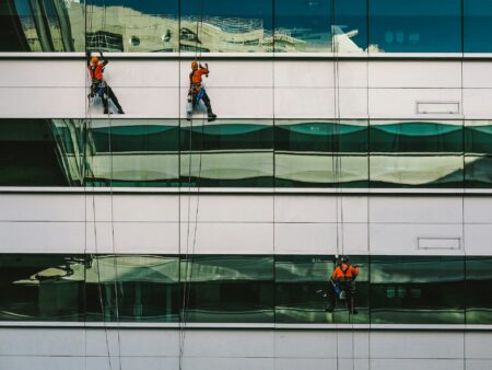 Drei Menschen reinigen die Fassade eines Bürokomplexes.