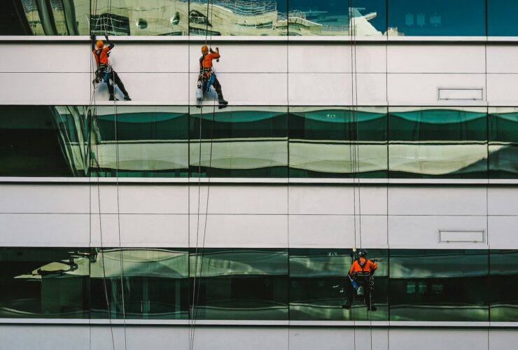 Drei Menschen reinigen die Fassade eines Bürokomplexes.